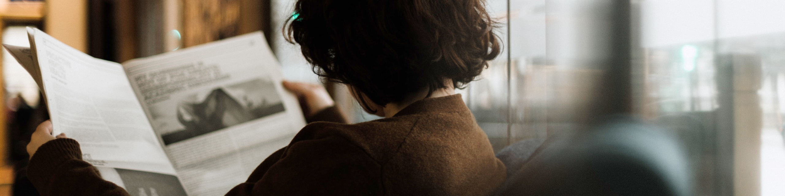 女性が新聞を読んでいる後ろ姿の写真